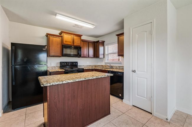 Kitchen featuring black appliances, a sink, a kitchen island, light tile patterned floors, and light stone counters | Image 8