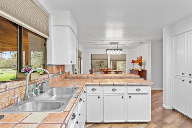 Kitchen with hanging light fixtures, white cabinetry, tile counters, and sink | Image 12