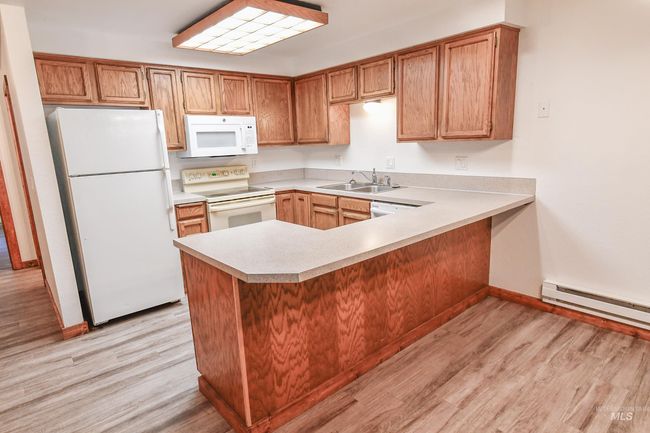 Kitchen featuring white appliances, light countertops, light wood-style floors, baseboard heating, and a peninsula | Image 11
