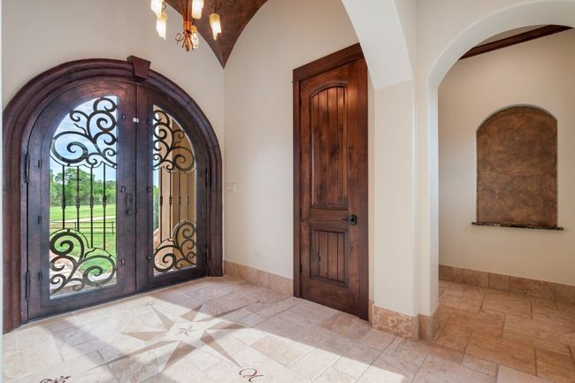 Foyer entrance with arched walkways, wrought iron doors, stone tile floors, & vaulted ceiling. | Image 6
