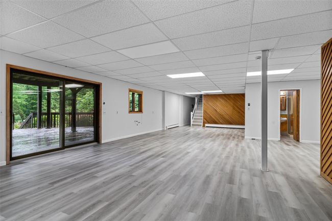 Unfurnished living room featuring a baseboard heating unit, a drop ceiling, wood finished floors, and stairs | Image 25