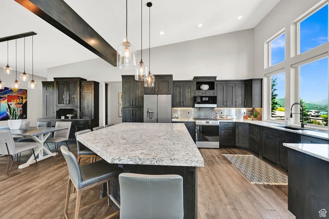 Kitchen featuring GE Cafe Platinum Glass appliances, high vaulted ceiling, light countertops, a center island, and tasteful backsplash | Image 21
