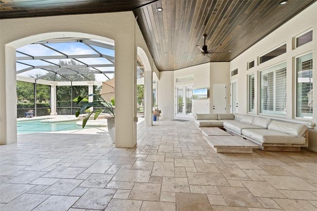 The expansive covered lanai features elegant stone flooring, a wood-paneled ceiling with recessed lighting, and seamless access to the screened-in pool—perfect for year-round outdoor living. | Image 25