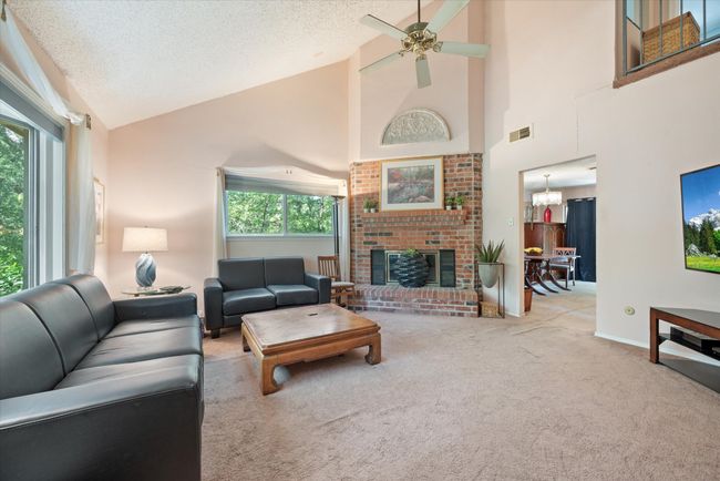 Living room featuring light carpet, a brick fireplace, ceiling fan with notable chandelier, a textured ceiling, and high vaulted ceiling | Image 15