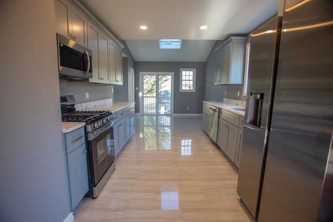 Kitchen featuring appliances with stainless steel finishes, gray cabinets, light stone counters, and lofted ceiling with skylight | Image 9