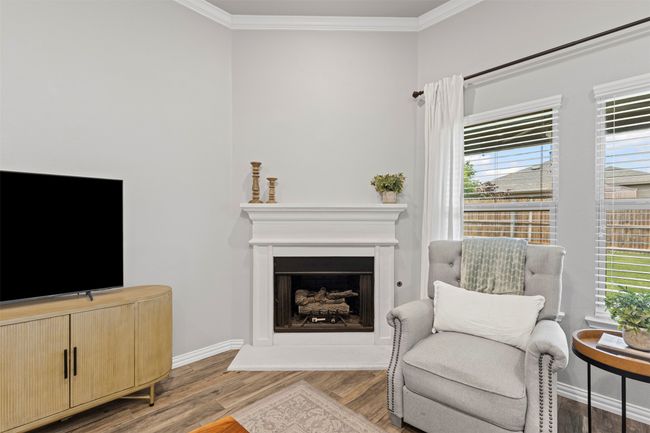 Living area featuring crown molding, wood like tile floors, and a fireplace with raised hearth | Image 24