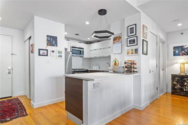 Kitchen featuring light hardwood / wood-style floors, white cabinetry, decorative light fixtures, kitchen peninsula, and stainless steel appliances | Image 6