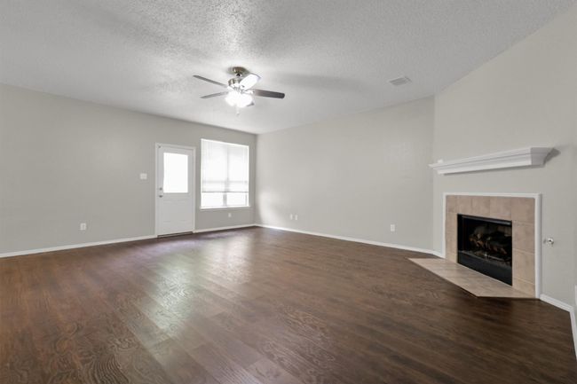 Unfurnished living room featuring ceiling fan, a textured ceiling, a fireplace, wood finished floors, and baseboards | Image 7