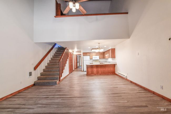 Unfurnished living room featuring light wood finished floors, a chandelier, stairs, a ceiling fan, and a high ceiling | Image 7