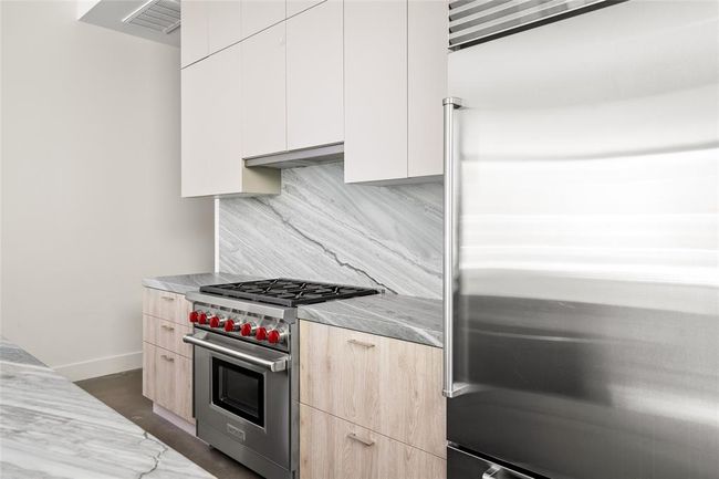 This designer kitchen is outfitted with top-tier Wolf and Sub-Zero appliances, set against a backdrop of striking honed Quartzite counters and full-height backsplash. Warm wood cabinetry softens the sleek lines, while the signature Wolf red knobs add a bold, iconic touch—delivering both high performance and visual impact in a beautifully streamlined space. | Image 16