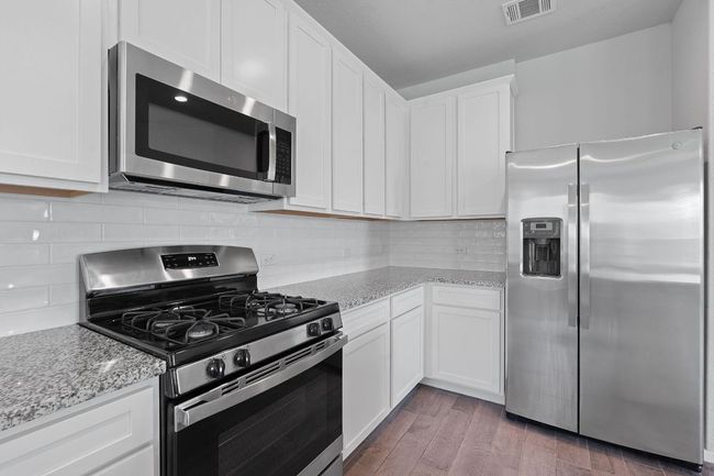 Kitchen with stainless steel appliances, white cabinets, light stone counters, and wood finished floors | Image 12