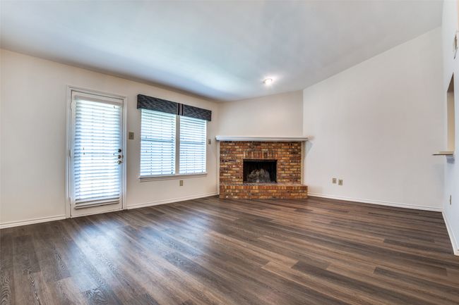 Unfurnished living room featuring a brick fireplace and dark wood-type flooring | Image 5