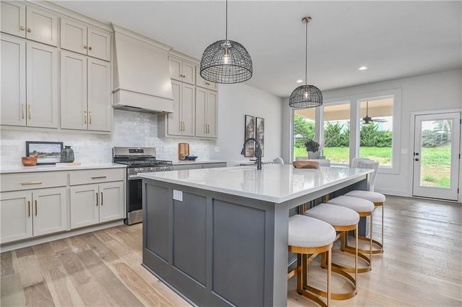 Kitchen featuring stainless steel gas range, light wood-type flooring, premium range hood, and a center island with sink | Image 14