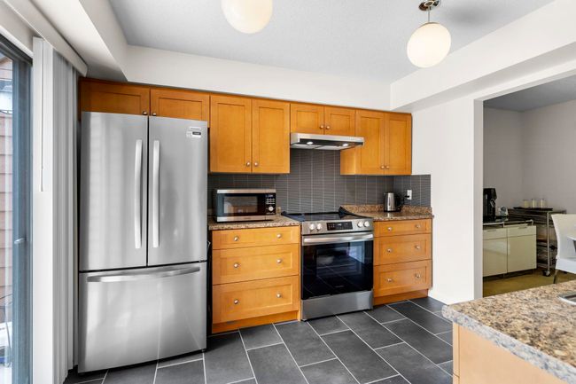 Kitchen with stainless steel appliances, under cabinet range hood, tasteful backsplash, brown cabinetry, and dark tile patterned floors | Image 12