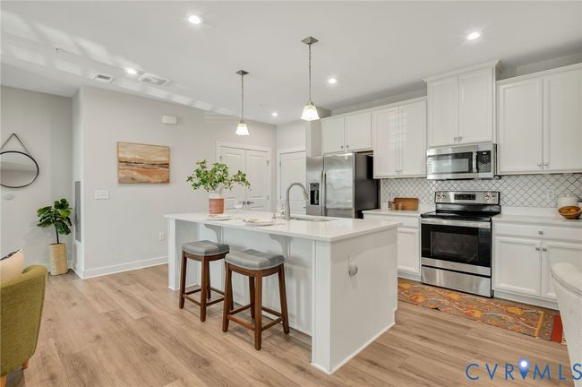 Kitchen featuring stainless steel appliances, decorative backsplash, a center island with sink, white cabinets, and light wood finished floors | Image 6