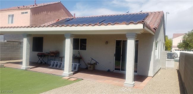 Rear view of house with roof mounted solar panels, a patio area, stucco siding, and a tile roof | Image 13