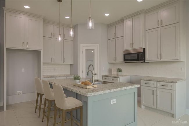 Kitchen with stainless steel microwave, a center island with sink, decorative backsplash, a kitchen bar, and hanging light fixtures | Image 25