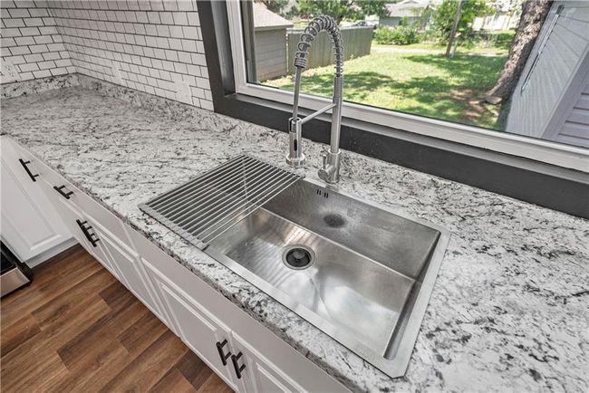 Kitchen view of a sink, white cabinetry, dark wood-style flooring, tasteful backsplash, and light countertops | Image 20