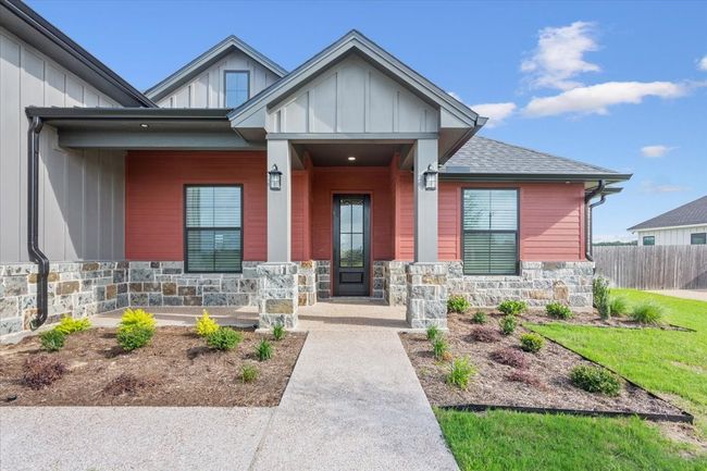 View of exterior entry with stone siding, covered porch, board and batten siding, and a shingled roof | Image 4