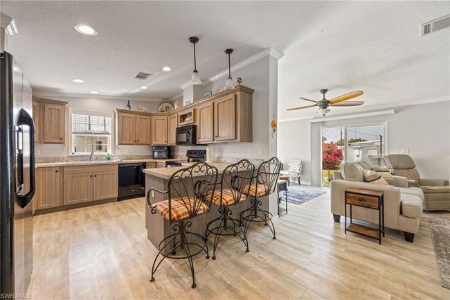 Kitchen with a textured ceiling, crown molding, black appliances, open floor plan, and a peninsula | Image 11