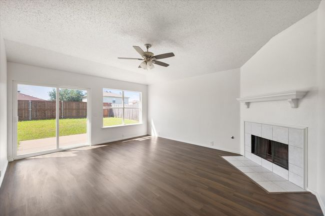 Computer staged den/iving area with a tile fireplace, ceiling fan, wood finished floors, and a textured ceiling | Image 9