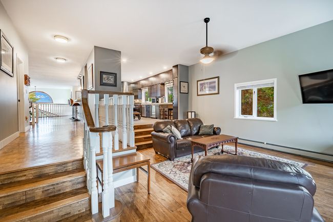 Living room with wood finished floors, a baseboard heating unit, stairway, and ceiling fan | Image 15