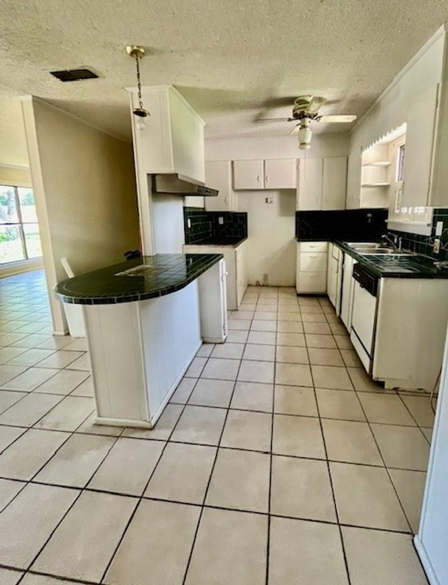 Kitchen with white dishwasher, light tile patterned floors, a textured ceiling, ceiling fan, and white cabinets | Image 4