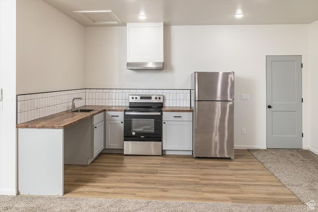 Kitchen featuring wooden counters, appliances with stainless steel finishes, light wood-type flooring, sink, and range hood | Image 37