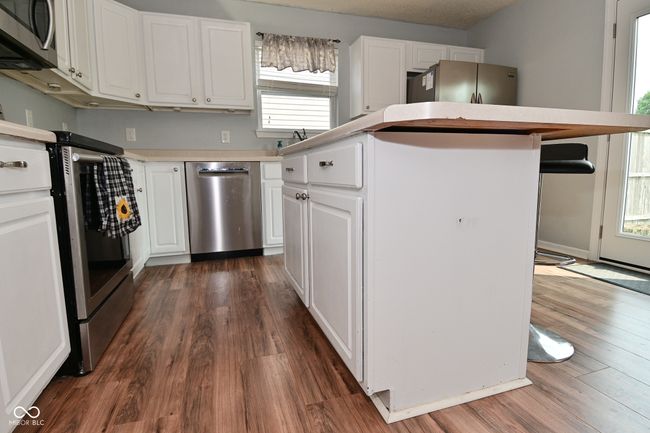kitchen with appliances with stainless steel finishes, dark wood-type flooring, white cabinetry, and a kitchen island | Image 20