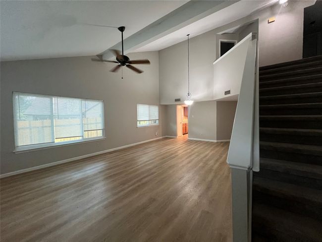Unfurnished living room with ceiling fan, baseboards, stairs, wood finished floors, and high vaulted ceiling | Image 8