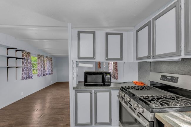 Kitchen with stainless steel gas range, black microwave, wood finished floors, light countertops, and white cabinetry | Image 13