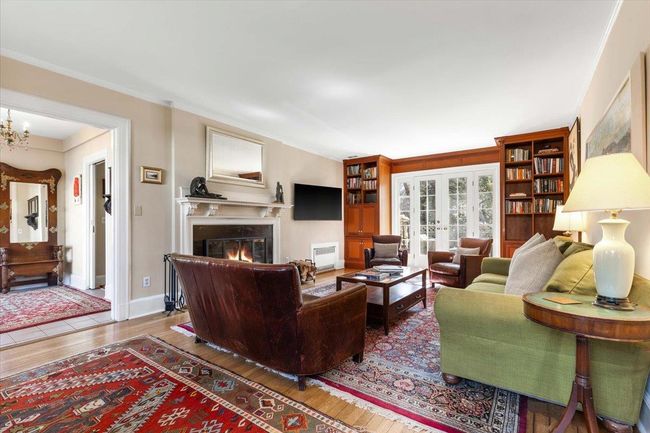Living room with french doors, ornamental molding, wood finished floors, a warm lit fireplace, and baseboards | Image 4