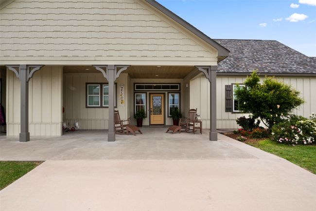 View of exterior entry with covered porch, a shingled roof, and board and batten siding | Image 6