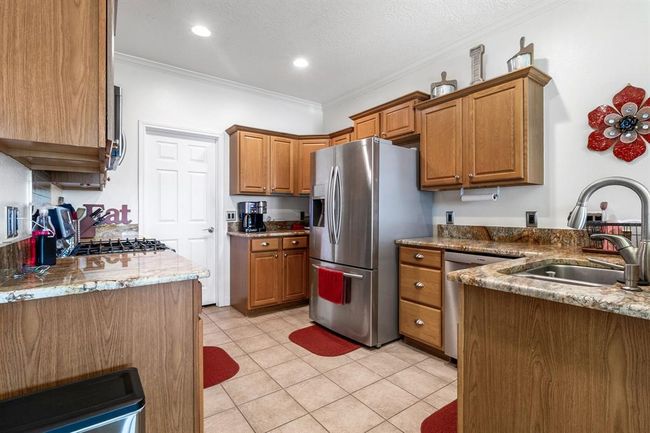 This kitchen features warm wooden cabinetry, granite countertops, and stainless steel appliances. It has a tiled floor, modern lighting, and a cozy, inviting atmosphere. | Image 11