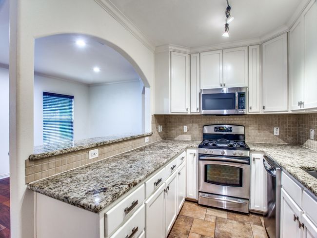 Kitchen featuring white cabinets, arched walkways, backsplash, and stainless steel appliances | Image 12