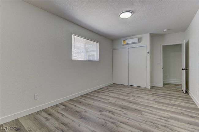 Unfurnished bedroom featuring a textured ceiling, light wood-type flooring, baseboards, a wall mounted air conditioner, and a closet | Image 27
