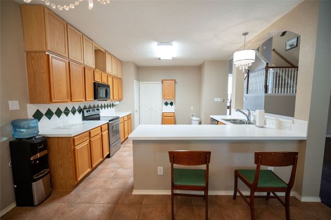 Kitchen featuring stainless steel range with electric stovetop, black microwave, a peninsula, a kitchen bar, and backsplash | Image 9