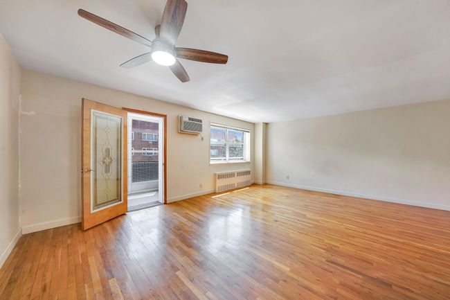 Unfurnished room with radiator heating unit, light wood-style flooring, baseboards, an AC wall unit, and ceiling fan | Image 4