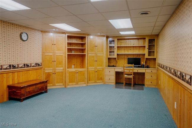 Carpeted basement featuring wallpapered walls, built in desk, a wainscoted wall, and wood walls | Image 28