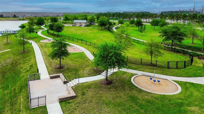 This photo showcases a spacious, well-maintained park with winding pathways, lush green lawns, and scattered trees. There's a playground area and a scenic view of a nearby water body, making it ideal for families and outdoor activities. | Image 47