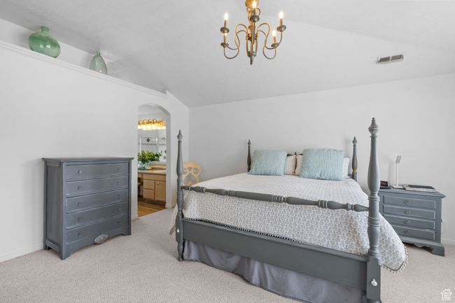 Carpeted bedroom featuring connected bathroom, arched walkways, a chandelier, lofted ceiling, and visible vents | Image 35