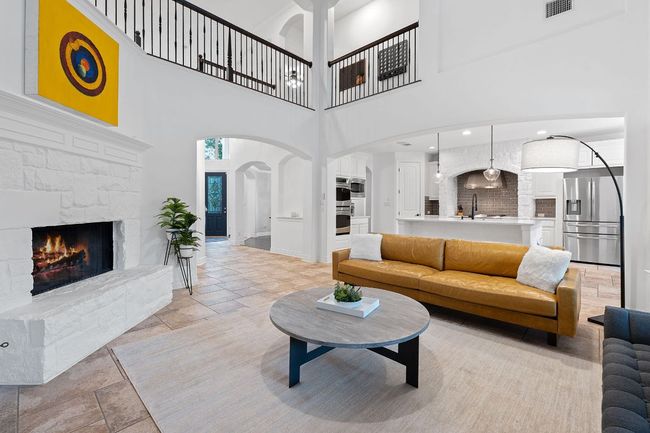 Living room featuring arched walkways, a stone fireplace, a towering ceiling, stone tile flooring, and baseboards | Image 10