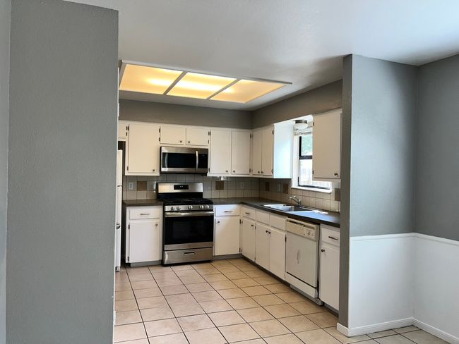 Kitchen with tasteful backsplash, appliances with stainless steel finishes, dark countertops, white cabinets, and a textured wall | Image 8