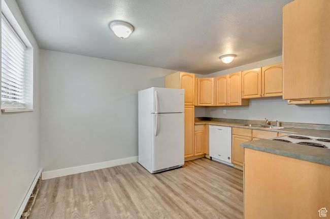 Kitchen featuring white appliances, light brown cabinetry, a sink, light wood-type flooring, and a baseboard radiator | Image 6