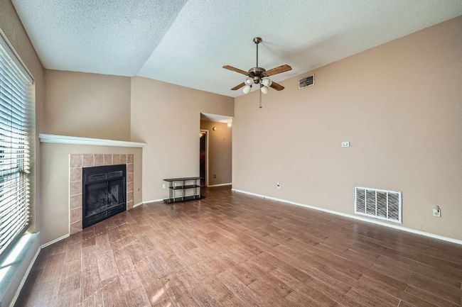 Unfurnished living room featuring ceiling fan, wood finished floors, a fireplace, a textured ceiling, and lofted ceiling | Image 6