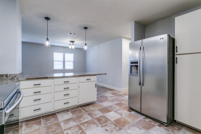 Kitchen with stainless steel appliances, a peninsula, white cabinets, light stone finish flooring, and hanging light fixtures | Image 12