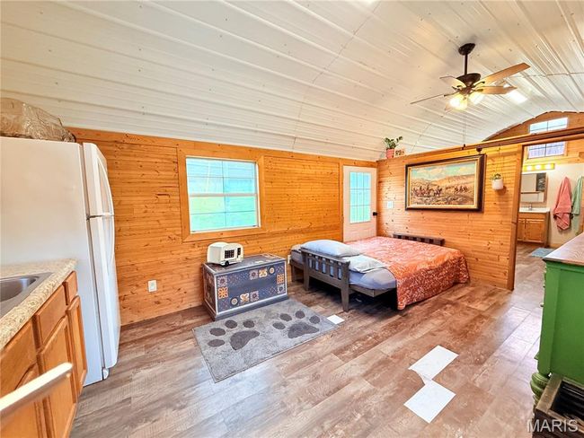 Bedroom featuring lofted ceiling, wooden walls, light wood-type flooring, multiple windows, and freestanding refrigerator | Image 19