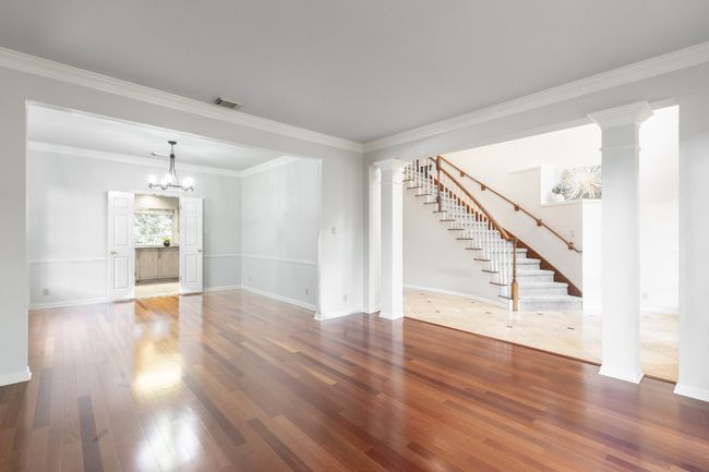 Unfurnished living room with ornate columns, stairs, hardwood / wood-style flooring, a chandelier, and ornamental molding | Image 20