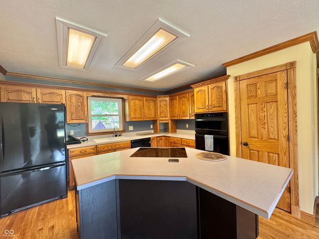 kitchen with black appliances, a sink, light countertops, a center island, and light wood finished floors | Image 44