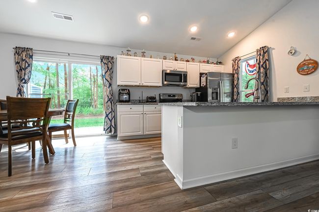 Kitchen with appliances with stainless steel finishes, dark stone counters, white cabinets, a peninsula, and dark wood finished floors | Image 6